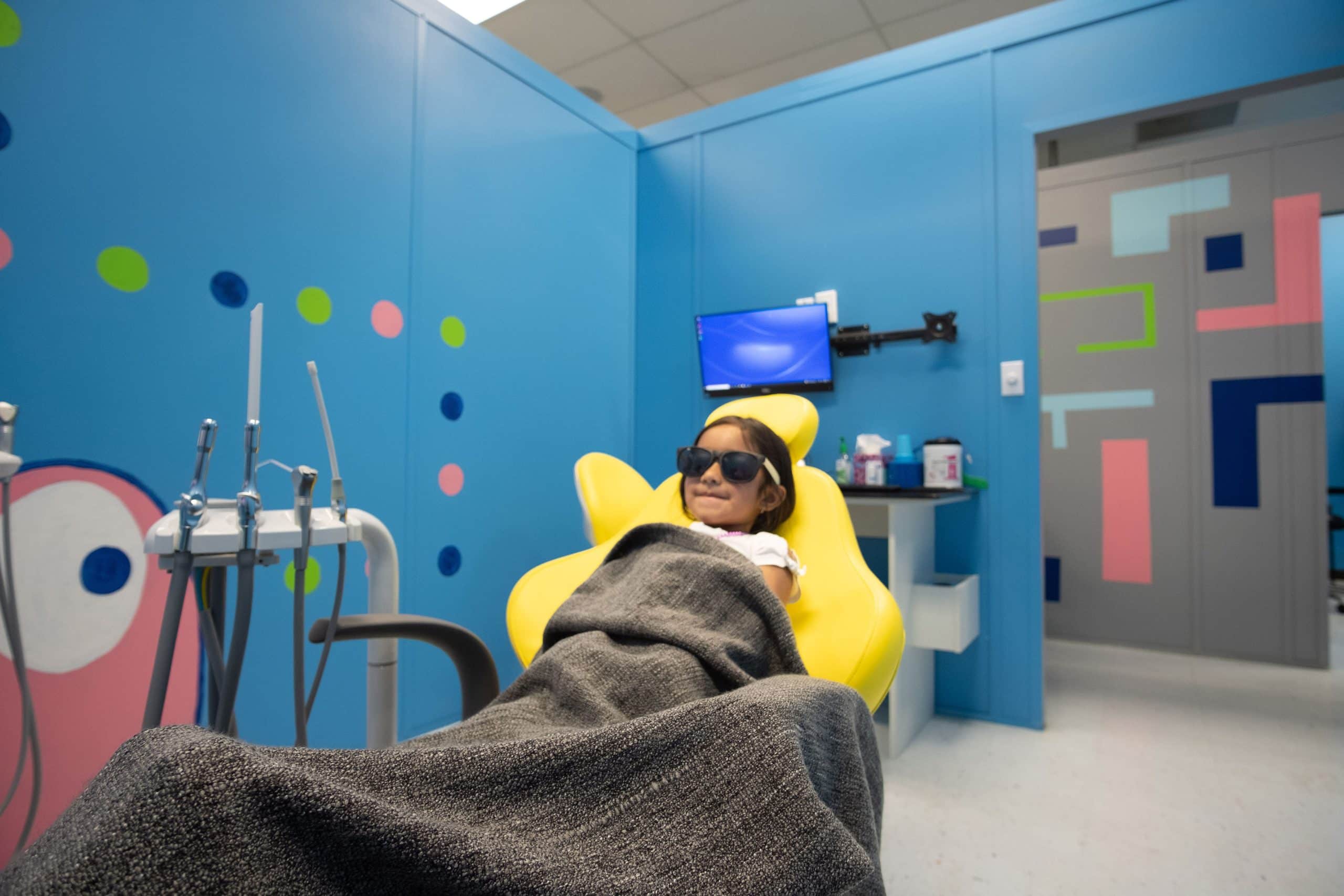child with blanket and glasses on dental chair